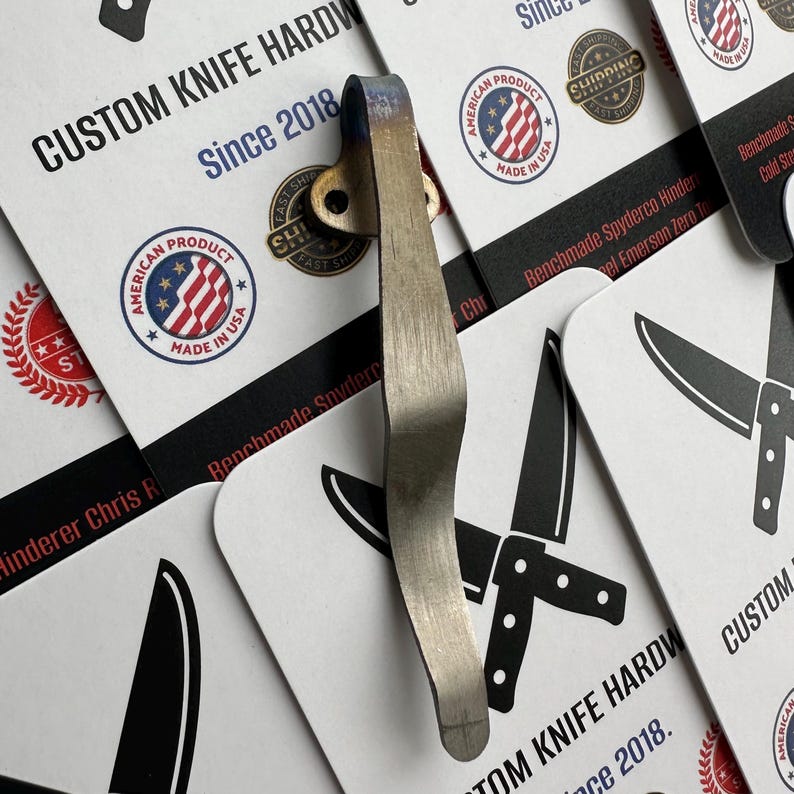 May include: A silver-colored knife clip with a brass-colored rivet is displayed against a backdrop of business cards. The cards feature the text "CUSTOM KNIFE HARDWARE Since 2018" and "AMERICAN PRODUCT MADE IN USA" logos.
