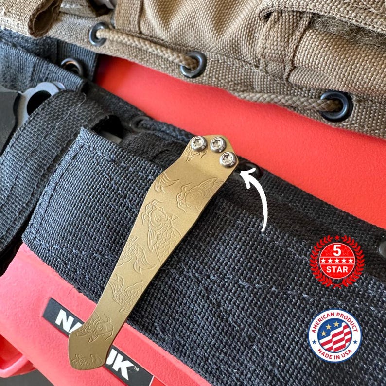 May include: A gold-colored pocket clip with an etched koi fish design, attached with three silver screws. The clip is mounted on a black fabric pocket with a red interior. The image also includes a "5 Star" and "American Product Made in USA" badge.
