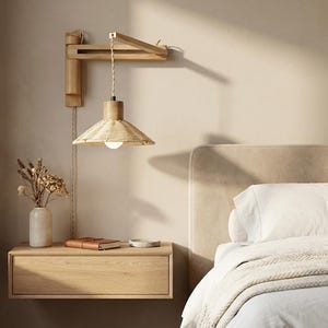 Pode incluir: Interior de quarto com uma luminária de parede de madeira e um abajur tecido, uma mesa de cabeceira flutuante e uma cama com roupa de cama branca. A luminária está acima da mesa de cabeceira, com um vaso de flores secas e um livro pequeno. Paleta de cores neutra.