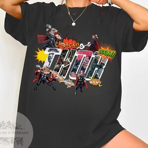 May include: Black t-shirt featuring a comic book style graphic of Thor with the word "THOR" in large, stylized letters. The design includes action bubbles with words like "CRACK!" and "BOOM!"