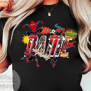 May include: Black t-shirt featuring a colorful graphic of Spider-Man in action poses with comic book sound effects. The word "TAT" is prominently displayed in a bold, comic-style font, with comic book panels inside the letters.