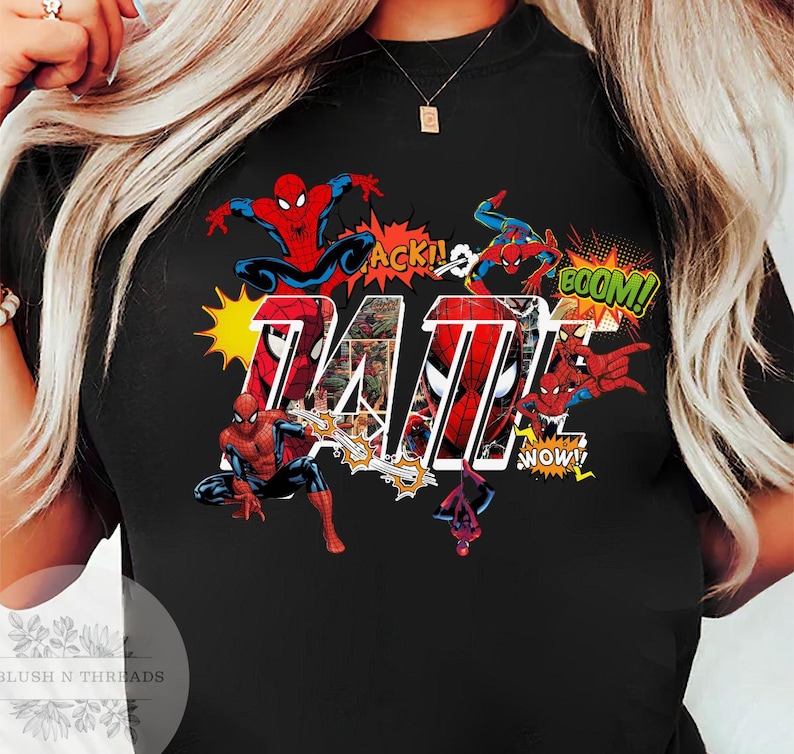 May include: Black t-shirt featuring a colorful graphic of Spider-Man in action poses with comic book sound effects. The word "TAT" is prominently displayed in a bold, comic-style font, with comic book panels inside the letters.