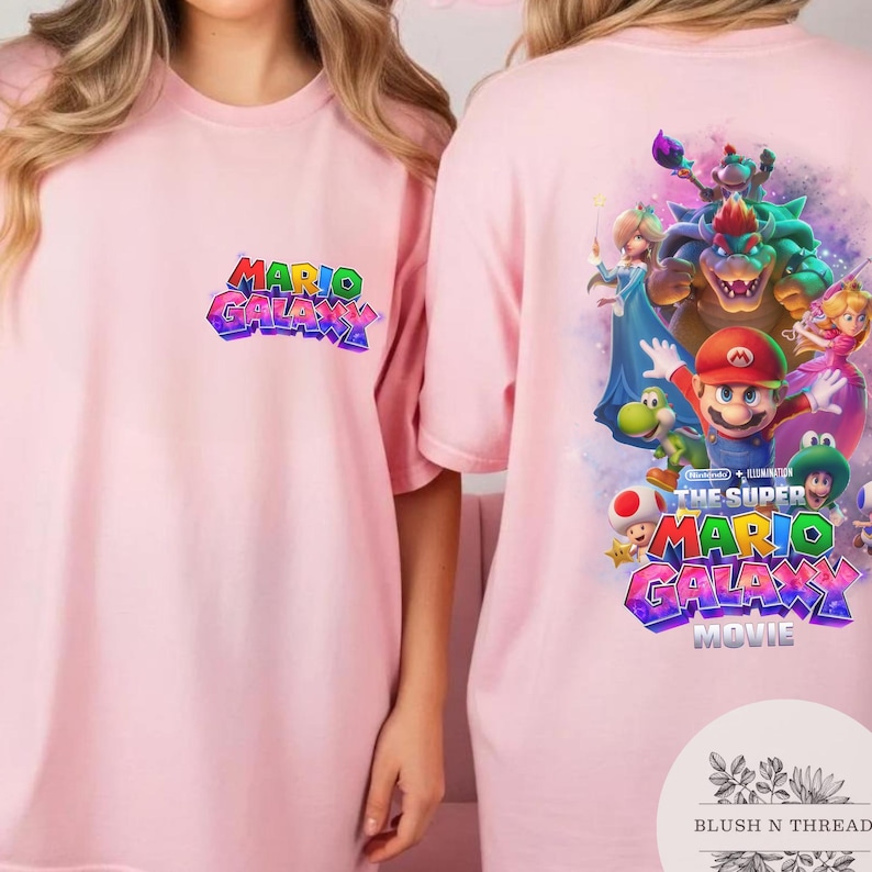 Puede incluir: Camiseta rosa claro con el texto "MARIO GALAXY" en letras coloridas en la parte delantera. La parte trasera de la camiseta muestra un gr&aacute;fico vibrante de Mario y otros personajes de la pel&iacute;cula Super Mario Galaxy.