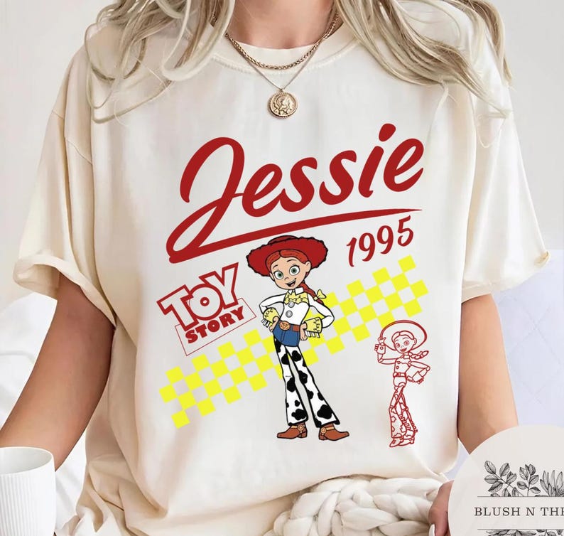 May include: Cream-colored t-shirt featuring a graphic of Jessie from Toy Story. The design includes the name "Jessie" in red script, the year "1995", and the Toy Story logo. A cartoon image of Jessie is also present.