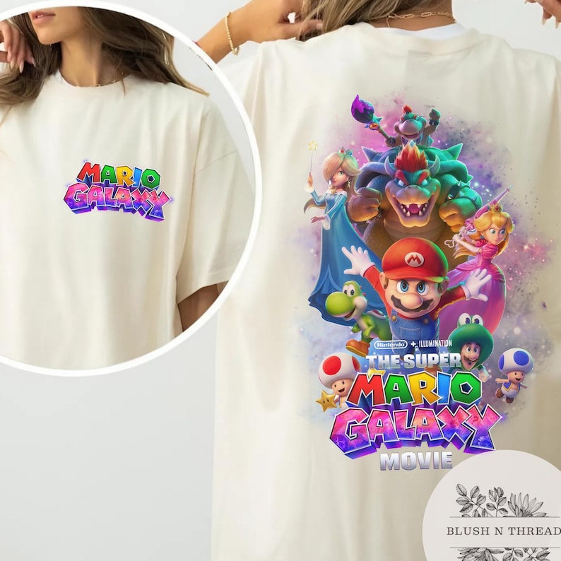Puede incluir: Camiseta color crema con el texto "MARIO GALAXY" en una fuente 3D colorida en la parte delantera. La parte posterior de la camiseta muestra un gr&aacute;fico vibrante de Mario y otros personajes de la pel&iacute;cula Super Mario Galaxy.