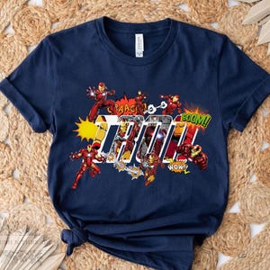 May include: Navy blue t-shirt featuring Iron Man in action poses with comic book sound effects. The word "Iron" is prominently displayed in a bold, stylized font, with "BOOM!" and "WOW!" exclamations.