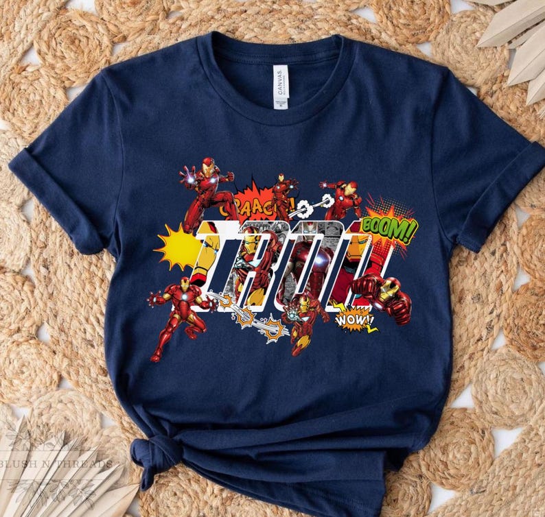 May include: Navy blue t-shirt featuring Iron Man in action poses with comic book sound effects. The word "Iron" is prominently displayed in a bold, stylized font, with "BOOM!" and "WOW!" exclamations.