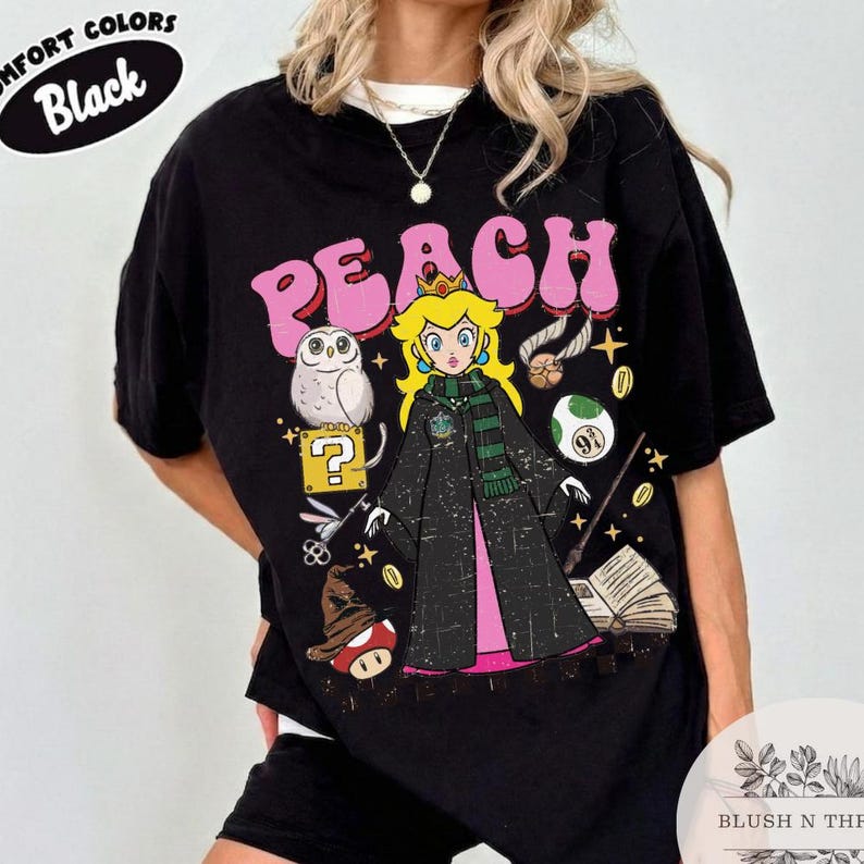 以下が含まれることがあります： 黒いTシャツ。プリンセスピーチがホグワーツ風の衣装を着たグラフィック、ピンク色の「PEACH」の文字、その他の漫画の要素が特徴です。このシャツには、フクロウ、疑問符、キノコも描かれています。