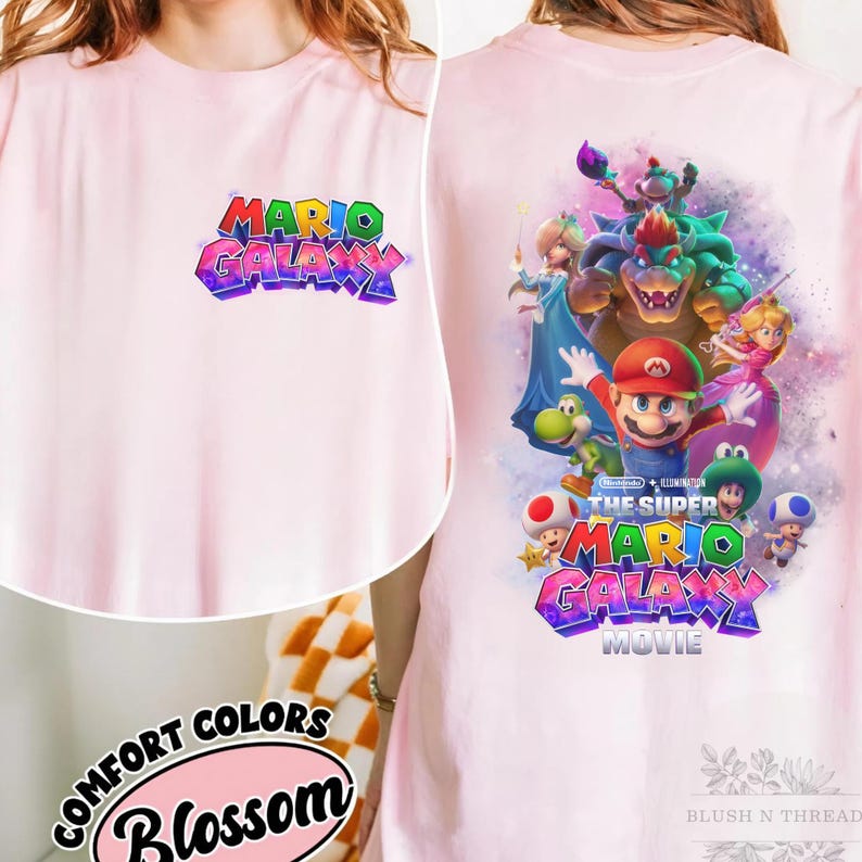 Puede incluir: Camiseta rosa claro con el texto "MARIO GALAXY" en un dise&ntilde;o 3D colorido en la parte delantera. La parte trasera de la camiseta muestra un gr&aacute;fico de Mario y otros personajes de la pel&iacute;cula Super Mario Galaxy. La camiseta es de Comfort Colors.