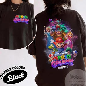 Puede incluir: Camiseta negra Comfort Colors con el texto "MARIO GALAXY" en la parte delantera y un gr&aacute;fico colorido de Mario y otros personajes de la pel&iacute;cula en la parte trasera. La camiseta tambi&eacute;n tiene el texto "THE SUPER MARIO GALAXY MOVIE".