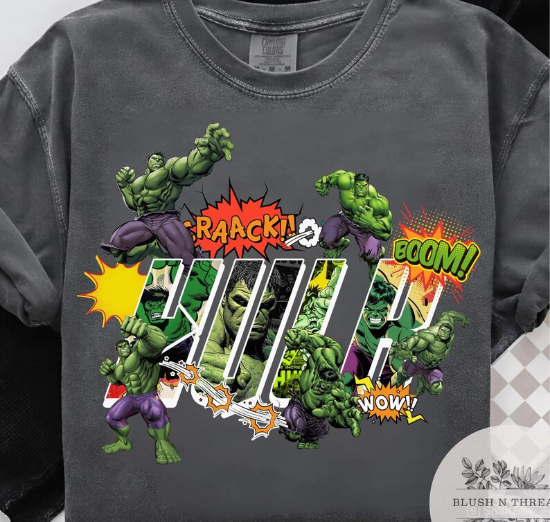 May include: Dark gray t-shirt featuring multiple illustrations of the Hulk in action poses. Comic book style with text bubbles that say "RAACK!", "BOOM!", and "WOW!". The word "HULK" is also displayed.