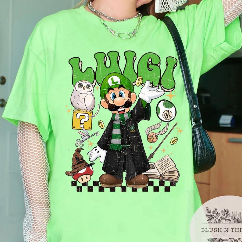 以下が含まれることがあります： レモンイエローのTシャツ。レトロなフォントで「Luigi」の文字と、魔法使いのローブとスカーフを着たルイージの漫画イラストが描かれています。デザインには、疑問符ブロック、フクロウ、その他の魔法の要素が含まれています。