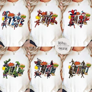 May include: White t-shirts featuring superhero names in a comic book style. Each shirt displays a different name: Steve, Thor, Jane, Hulk, Tirth, and Groot, with action-packed graphics and sound effects.