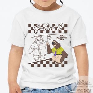 May include: White t-shirt featuring a cartoon graphic of two sloths from Zootopia. The design includes the word "Flask" above the sloths and the "Zootopia 2" logo. The shirt has a crew neck and short sleeves.