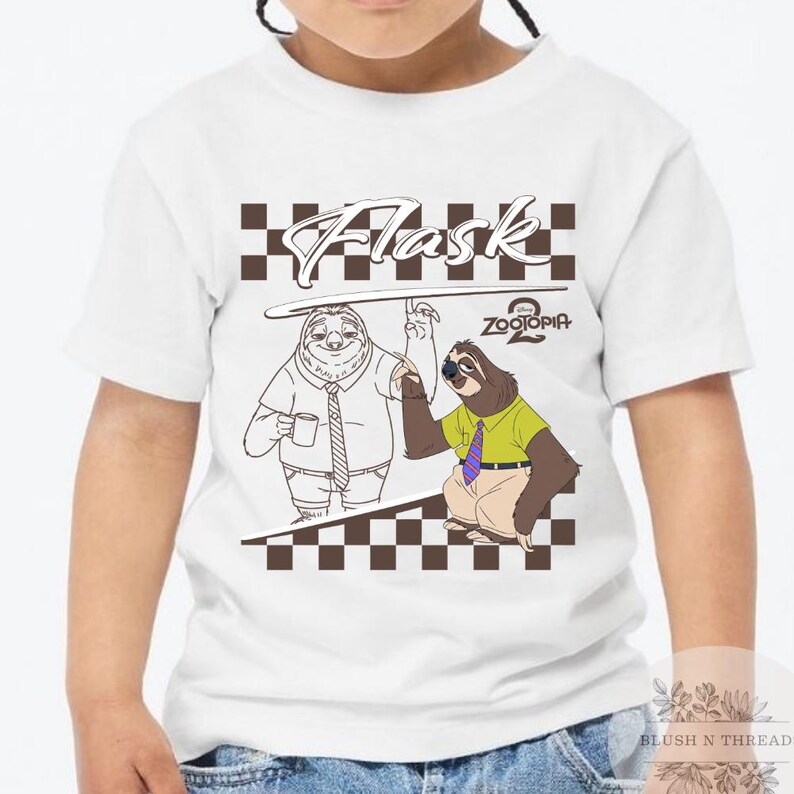 May include: White t-shirt featuring a cartoon graphic of two sloths from Zootopia. The design includes the word "Flask" above the sloths and the "Zootopia 2" logo. The shirt has a crew neck and short sleeves.