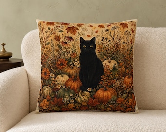 May include: A square throw pillow featuring a detailed print of a black cat sitting amidst a patch of orange, green, and white pumpkins, surrounded by autumn foliage, dried wildflowers, and fallen leaves in shades of brown, gold, and rust.