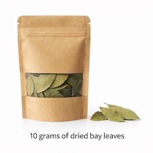 Op de afbeelding: Een bruine papieren zak met een doorzichtig venster, gevuld met gedroogde laurierbladeren. De zak is aan de bovenkant verzegeld en staat op een witte ondergrond. De tekst "10 gram gedroogde laurierbladeren" staat eronder.