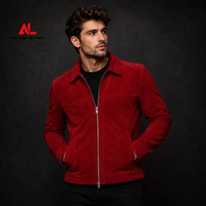 May include: A vibrant red suede jacket featuring a classic collar, a full-length silver-toned front zipper, and two side pockets. The garment is worn over a black shirt. The logo ARTISTIC LEATHER with the letters AL is visible in the top left corner.