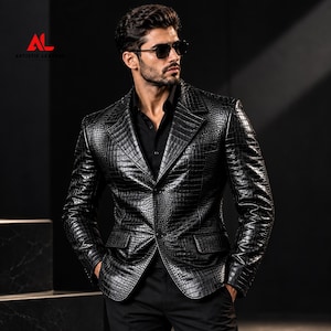 Puede incluir: Una americana negra con textura de piel de cocodrilo brillante, con solapa de muesca, dos botones frontales y dos bolsillos con solapa. La prenda se lleva sobre una camisa negra. El logotipo ARTISTIC LEATHER es visible en la esquina superior izquierda.
