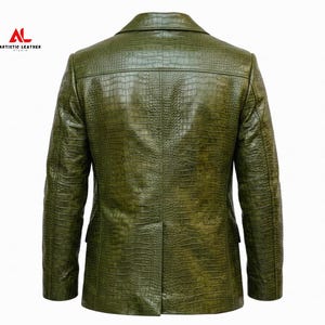 May include: An olive green blazer with a textured crocodile skin pattern. The back view shows a structured collar, long sleeves, and a single center vent at the hem. The logo ARTISTIC LEATHER STUDIO is printed in red and black in the upper left corner.