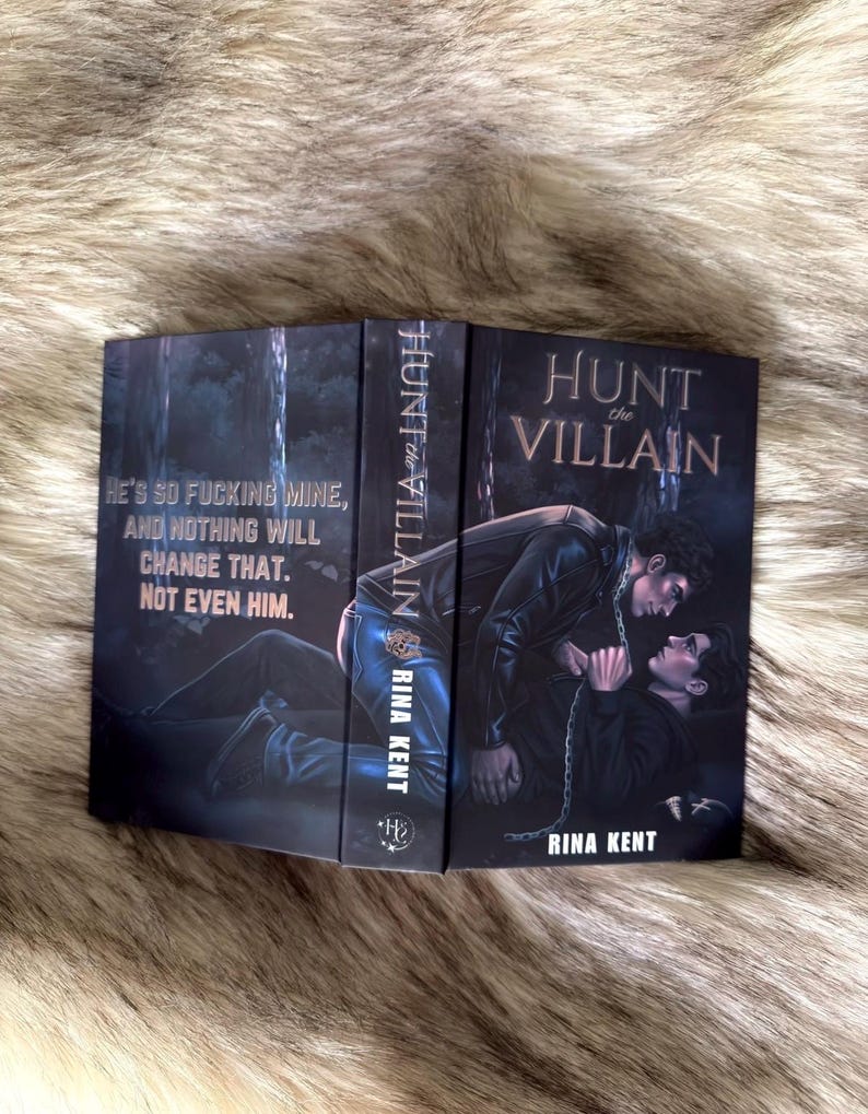 K&ouml;nnte beinhalten: Ein Buch mit dem Titel "Hunt the Villain" von Rina Kent. Das Cover zeigt eine dunkle Illustration von zwei M&auml;nnern in einem Wald. Der Titel und der Name des Autors sind zu sehen, sowie das Zitat: "He's so fucking mine, and nothing will change that. Not even him."