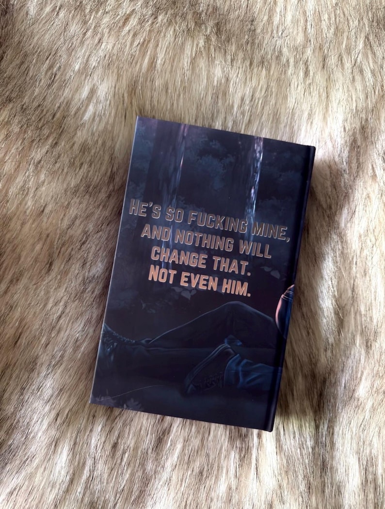 K&ouml;nnte beinhalten: Ein Buch mit dunklem Einband mit dem Text "HE'S SO FUCKING MINE, AND NOTHING WILL CHANGE THAT. NOT EVEN HIM." Das Cover zeigt eine dunkle Waldszene mit einer liegenden Person.