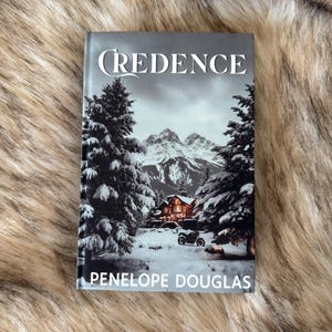 May include: A book titled "Credence" by Penelope Douglas. The cover features a snowy mountain scene with evergreen trees, a cabin, and a vehicle. The title is in a white, stylized font.