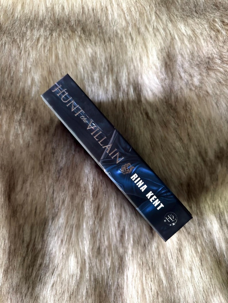 K&ouml;nnte beinhalten: Ein Buch mit dem Titel "Hunt the Villain" von Rina Kent. Das Buch hat einen dunklen Einband mit blauen und silbernen Akzenten. Der Name des Autors ist in Wei&szlig; gehalten. Das Buch ist rechteckig und scheint ein Taschenbuch zu sein.