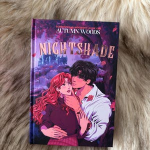 Può includere: Un libro intitolato "Nightshade" con un'illustrazione di copertina di una coppia che si abbraccia. Il libro fa parte della serie "Autumn Woods". L'artwork della copertina presenta una donna con i capelli rossi e un uomo con una camicia bianca.