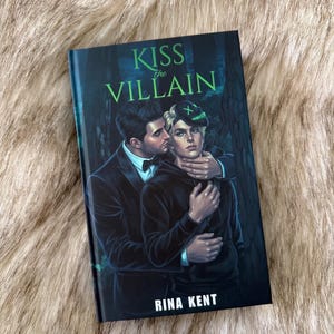 Pu&ograve; includere: Un libro con il titolo "KISS the VILLAIN" di Rina Kent. La copertina presenta un'illustrazione romantica di due persone che si abbracciano, una che bacia l'altra. Lo sfondo &egrave; una scena di foresta oscura con accenti verdi.