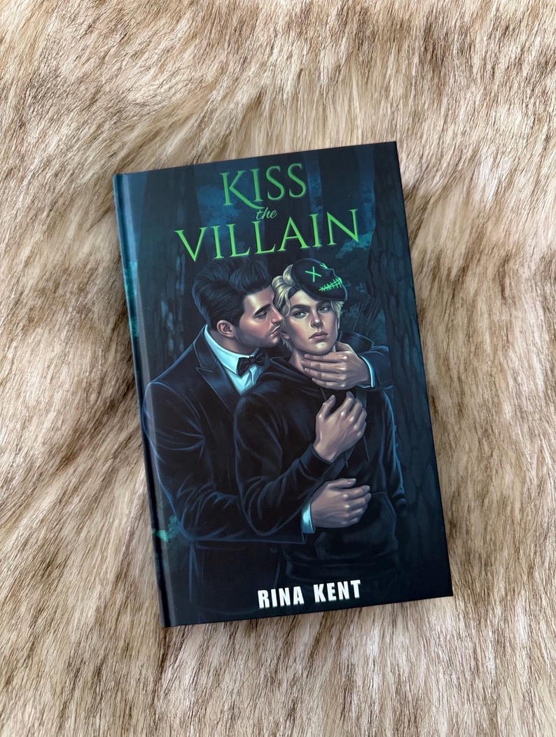 Pu&ograve; includere: Un libro con il titolo "KISS the VILLAIN" di Rina Kent. La copertina presenta un'illustrazione romantica di due persone che si abbracciano, una che bacia l'altra. Lo sfondo &egrave; una scena di foresta oscura con accenti verdi.