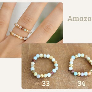 May include: Two elastic rings made of small, round, multi-colored amazonite beads interspersed with shiny gold-toned metallic spheres. The rings are labeled 33 and 34, featuring a mix of light blue, tan, brown, and cream-colored stone beads.