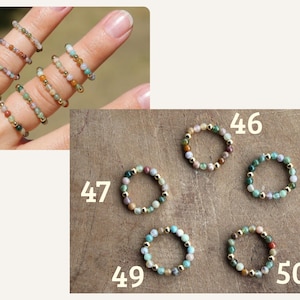 May include: A collection of elastic rings made from small, multicolored gemstone beads interspersed with tiny gold-toned metallic spheres. The rings are labeled with the numbers 46, 47, 48, 49, and 50, showcasing various color combinations of green, blue, and earth tones.
