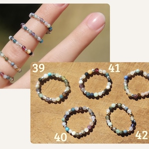 May include: A collection of five beaded rings labeled 39, 40, 41, 42, and 43. Each ring is crafted from small, multi-colored gemstone beads interspersed with tiny metallic silver or gold-toned spacer beads, creating a delicate, circular band design.