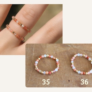May include: Two beaded rings featuring small, round, multi-colored gemstone beads in shades of orange, pink, and translucent white, interspersed with tiny metallic gold-tone spacer beads. The rings are labeled with the numbers 35 and 36.