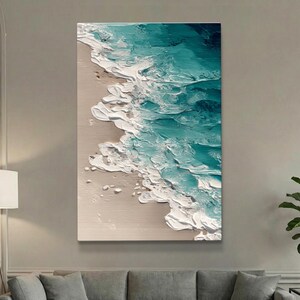 May include: A rectangular canvas art piece depicting an abstract ocean scene. The artwork features a textured application of white, teal, and dark blue paint, representing waves crashing on a sandy beach. The painting is displayed on a wall.