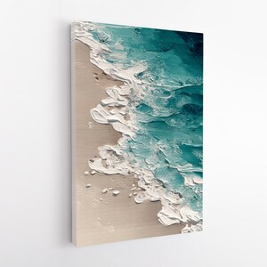May include: Textured canvas art depicting an aerial view of a beach scene. The artwork features a sandy beige shore with white foamy waves crashing against it. The ocean is rendered in shades of teal and turquoise.