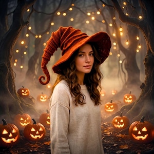 May include: A woman wearing a rust-colored, crocheted witch hat and a cream-colored sweater stands in a forest. Lit jack-o'-lanterns are scattered on the ground. The background features trees and soft, glowing lights, creating a Halloween theme.