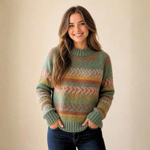 May include: A knitted sweater in shades of green, pink, and yellow, featuring a geometric pattern. The sweater has a crew neck and ribbed cuffs. The model is wearing dark blue jeans. The sweater's design includes chevron and horizontal stripes.