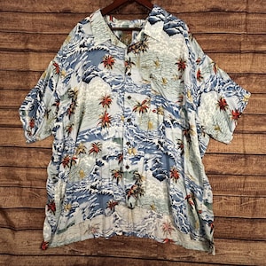May include: Light blue button-down shirt with a tropical print featuring palm trees, waves, and sailboats. The short-sleeved shirt has a classic collar and a single chest pocket. The shirt is hanging on a wooden hanger.