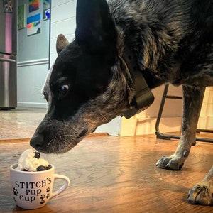 Dog eating from a personalized white pup cup with whipped cream and a blueberry