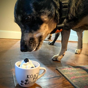 Dog eating from a personalized white pup cup with whipped cream and a blueberry