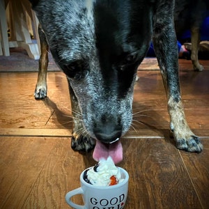 Dog eating from a personalized white pup cup with whipped cream and a blueberry