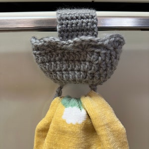 Gray crochet towel holder on oven door holding a yellow towel