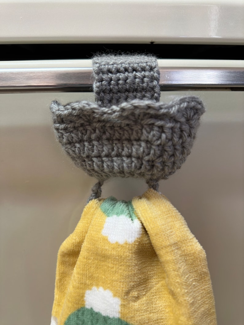 Gray crochet towel holder on oven door holding a yellow towel