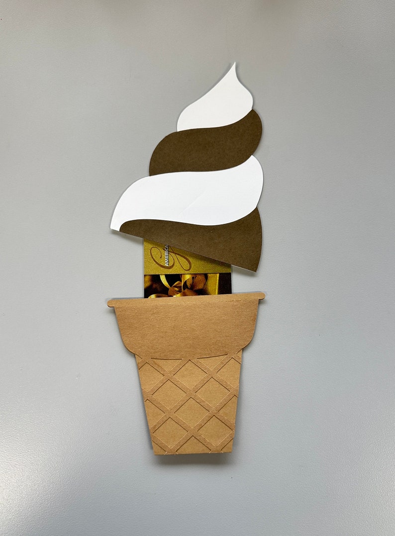 May include: A papercraft ice cream cone with a swirl of brown and white ice cream. The cone is made of brown paper with a waffle pattern. A gift card is visible inside the cone.