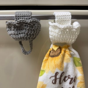 Crochet towel holders on an oven door. Gray towel holder on the left and white towel holder on the right holding a towel.