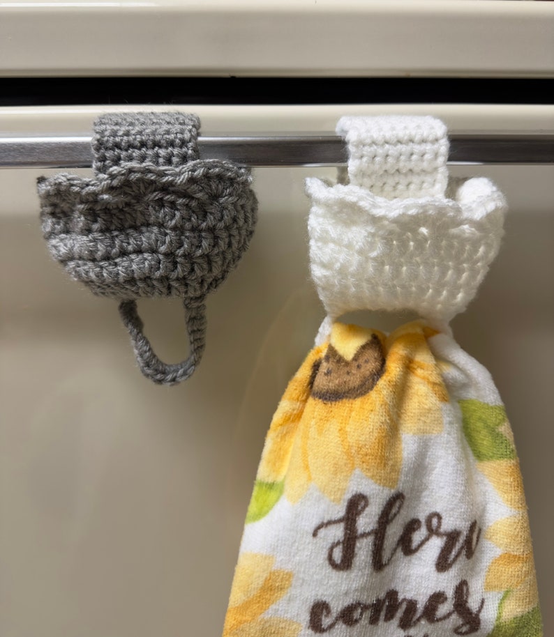 Crochet towel holders on an oven door. Gray towel holder on the left and white towel holder on the right holding a towel.