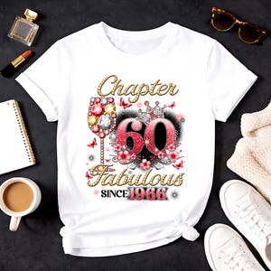 Może przedstawiać: Biała koszulka z kolorowym wzorem graficznym z okazji 60. urodzin. Projekt zawiera napisy "Chapter 60 Fabulous Since 1966" z kieliszkiem do wina, kwiatami i motylami.