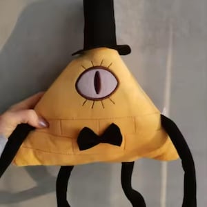 Könnte beinhalten: Ein gelbes, dreieckiges Plüschtier mit einem einzelnen Auge, einem schwarzen Zylinder und einer schwarzen Fliege. Es hat schwarze Arme und Beine. Das Auge ist weiß mit einer braunen Pupille und ist von gelben Strahlen umgeben.